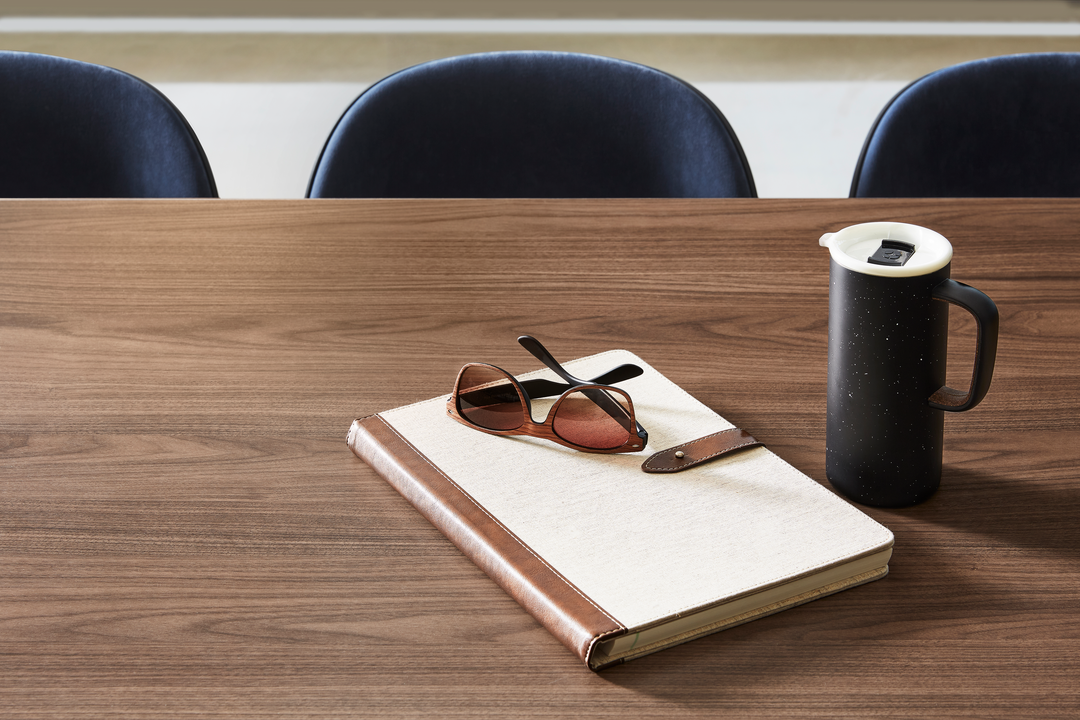 A woodgrain table with a notebook, sunglasses, and a thermos sitting on top.