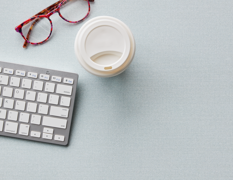 Coffee cup, keyboard and glasses on a pale blue laminate surface