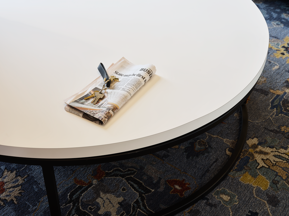 A white matte coffee table with a newspaper and keys on it