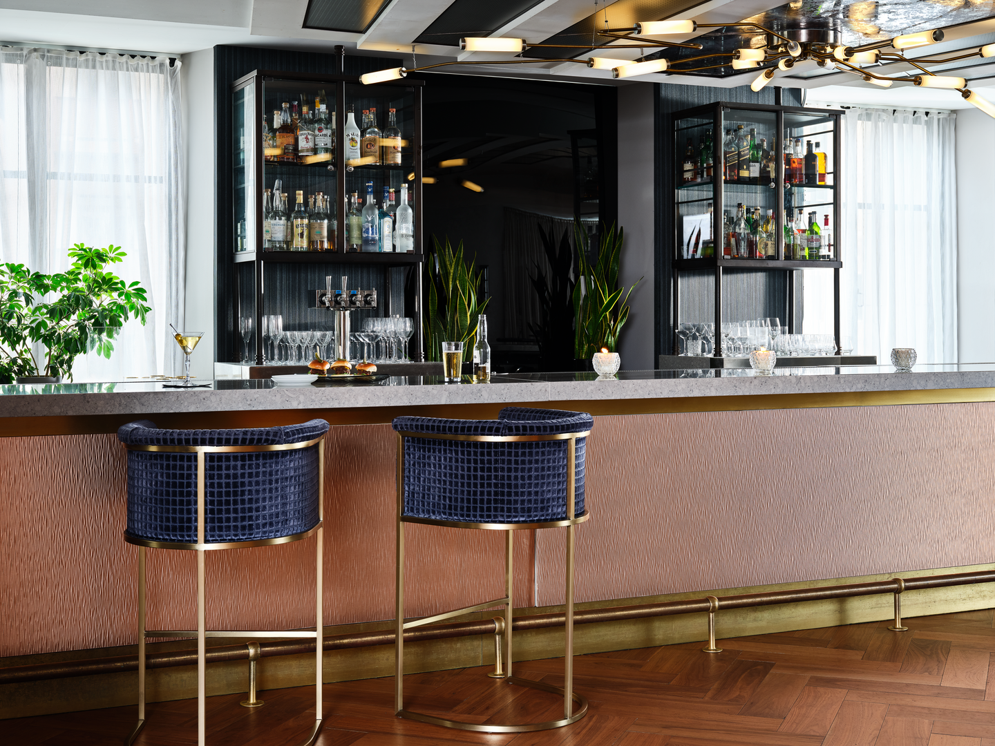 Un bar avec une devanture métallique brillante et des tabourets en velours bleu foncé
