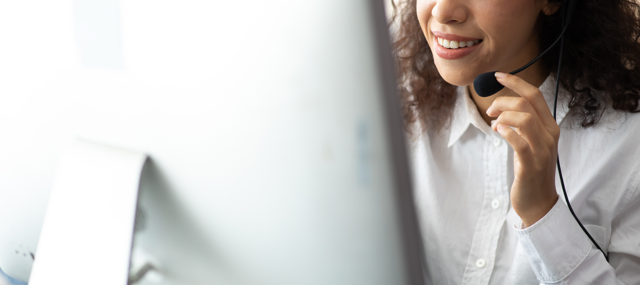 A smiling woman in customer service talking through a headset.