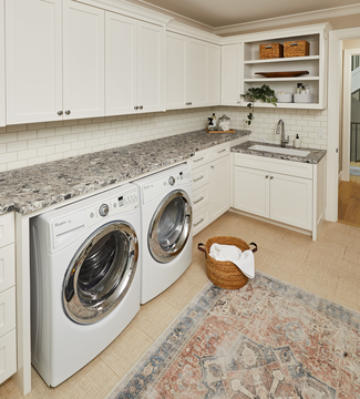 A home laundry room with speckled stone countertops and white cabinetry.