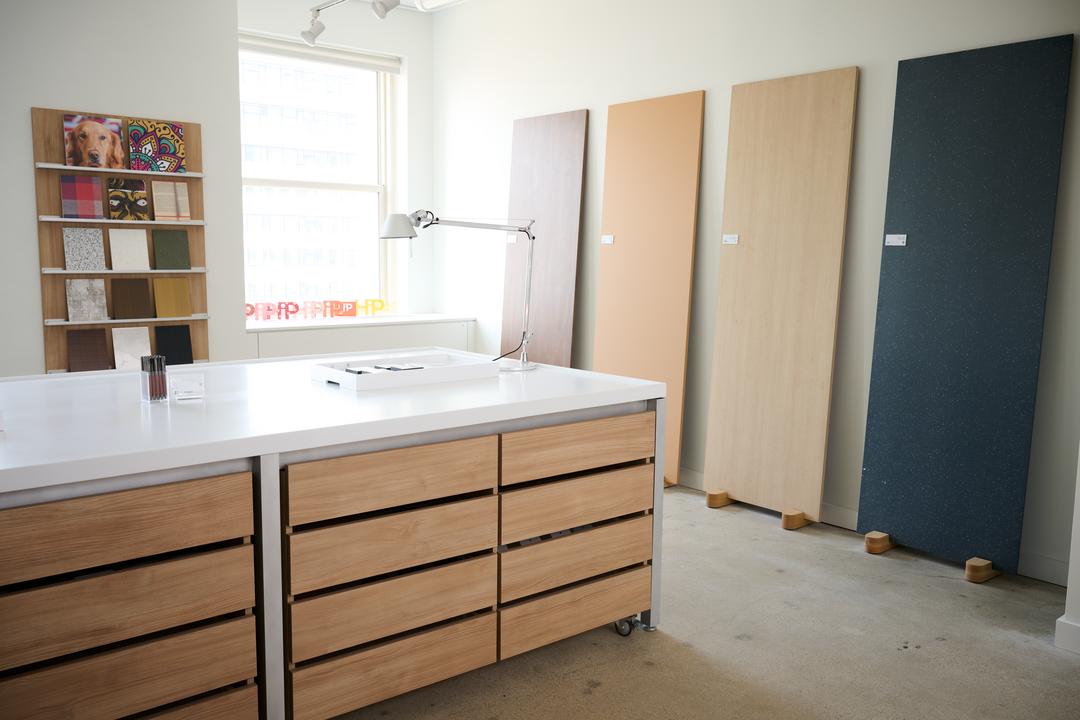 A worktable with wooden cabinets and a white top. Large panels leaning up against a wall.