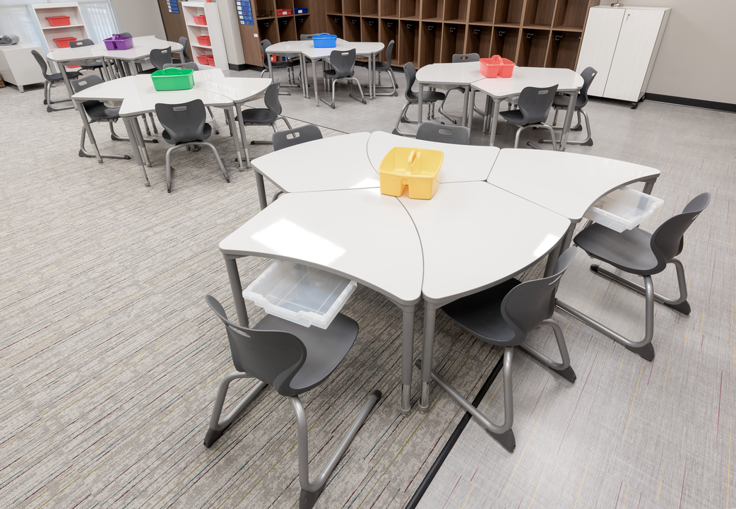 A classroom for your kids featuring short gray chairs and uniquely shaped markerboard desks